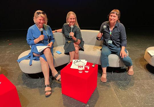 three women sitting on couch, holding microphones